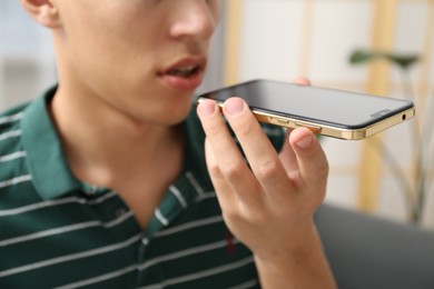 Photo of Young man recording voice message via smartphone at home, closeup