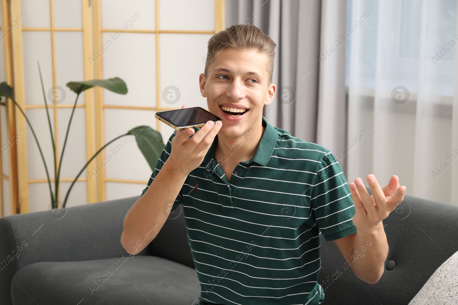 Photo of Young man recording voice message via smartphone at home