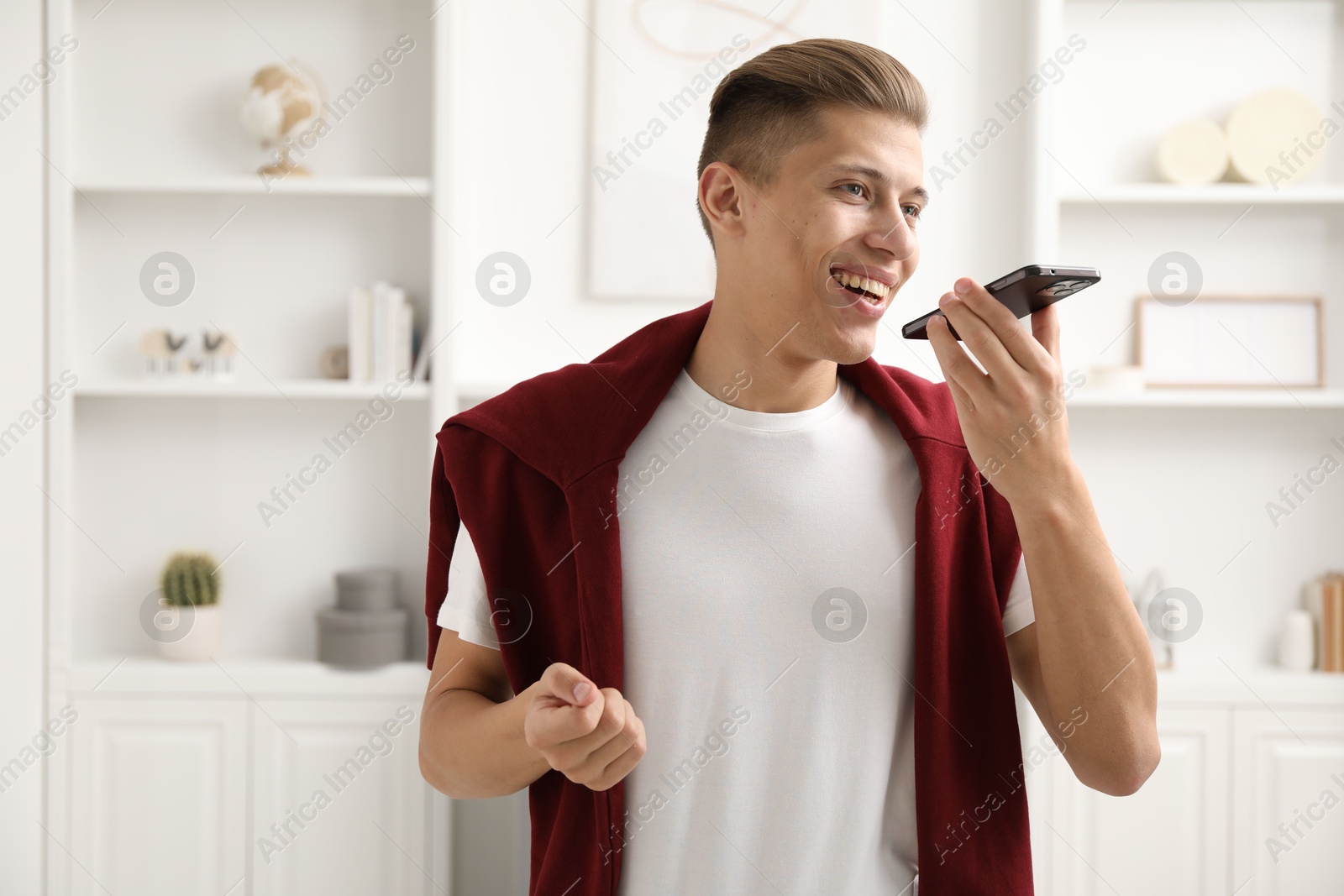 Photo of Young man recording voice message via smartphone at home