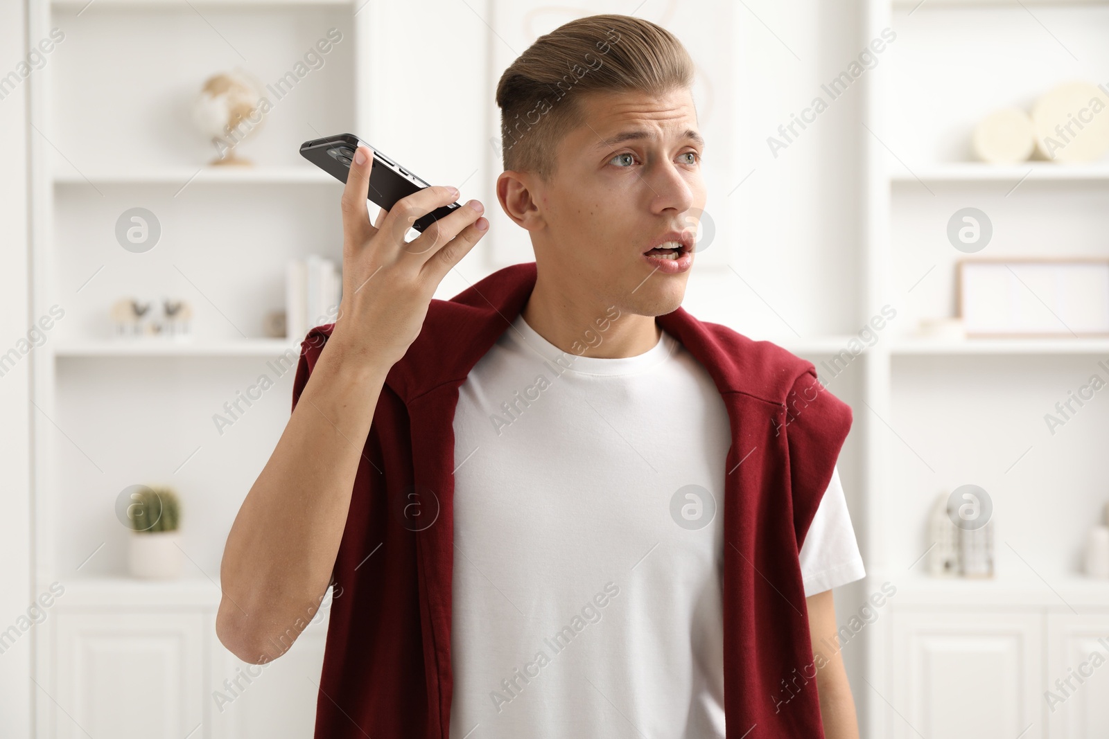 Photo of Young man with smartphone listening to voice message at home