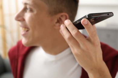 Photo of Young man with smartphone listening to voice message at home, selective focus