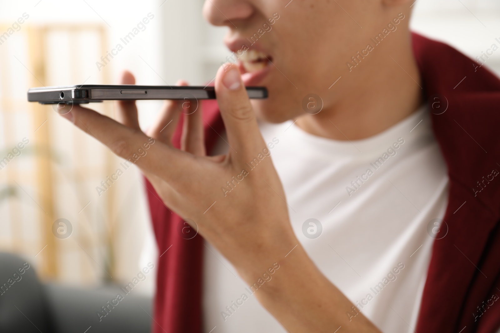 Photo of Young man recording voice message via smartphone at home, closeup