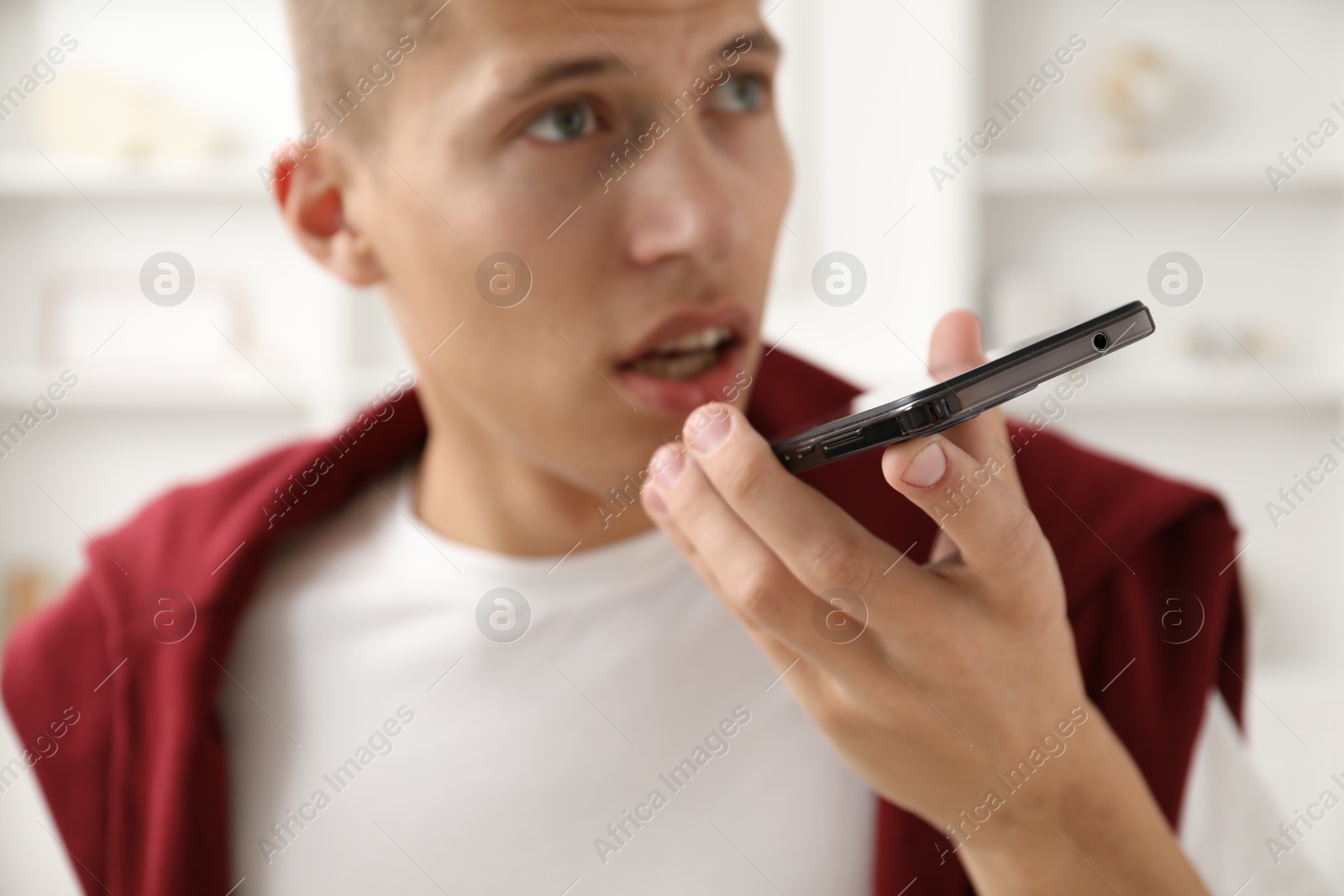 Photo of Young man recording voice message via smartphone at home, selective focus