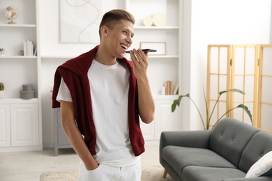 Photo of Young man recording voice message via smartphone at home