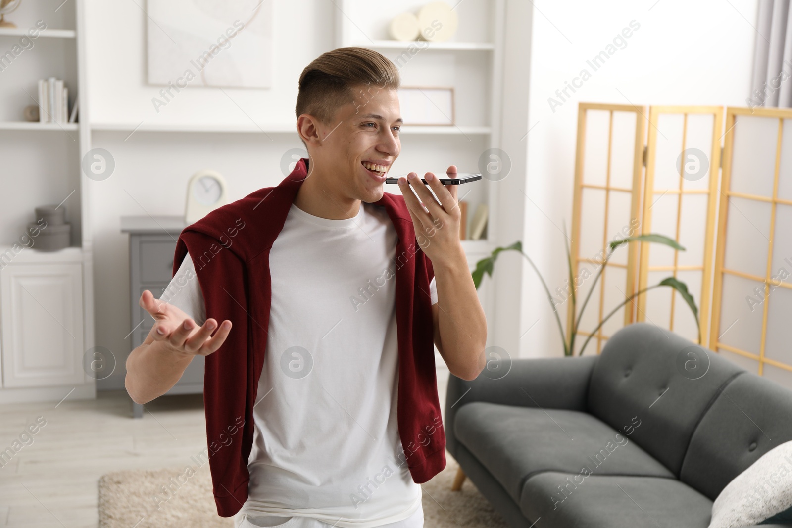 Photo of Young man recording voice message via smartphone at home