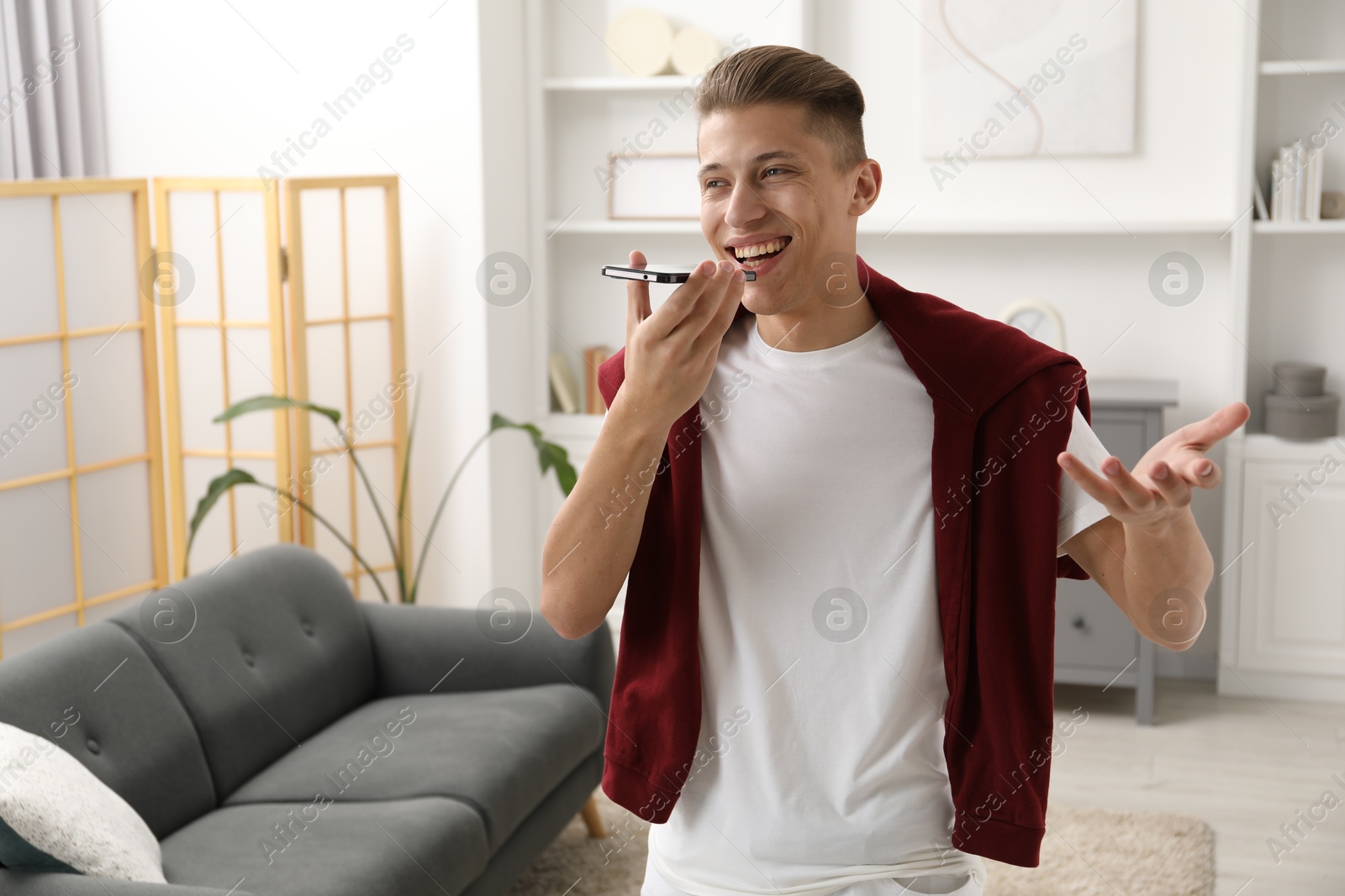 Photo of Young man recording voice message via smartphone at home