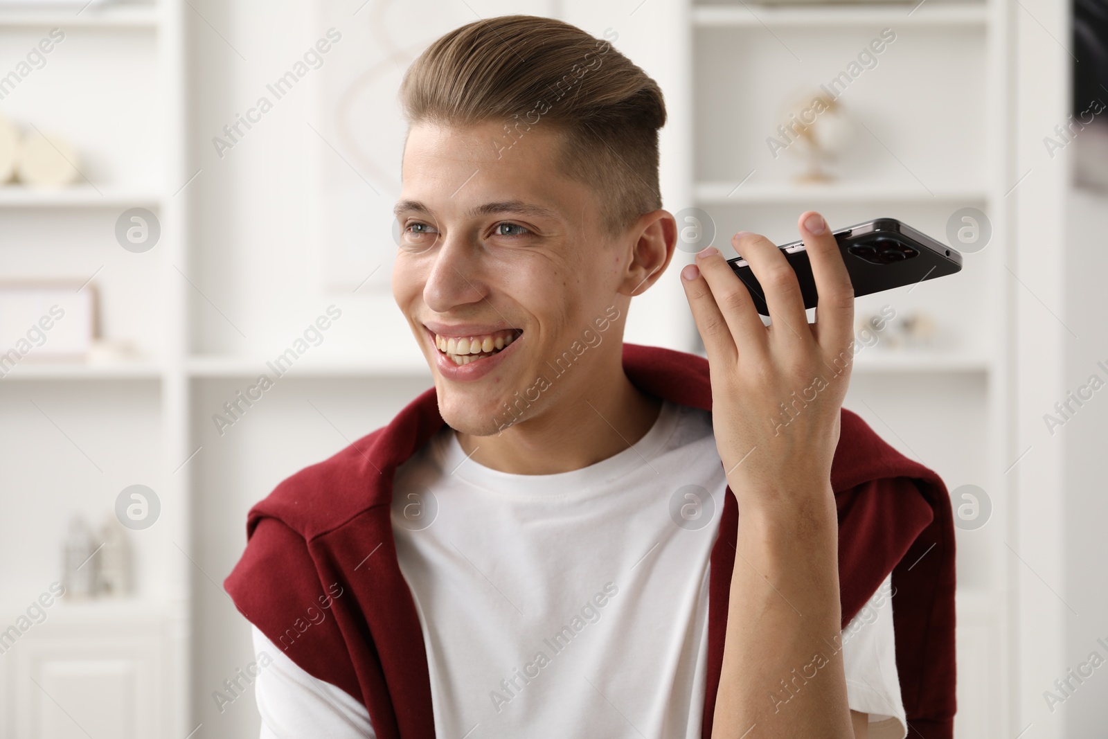 Photo of Young man with smartphone listening to voice message at home