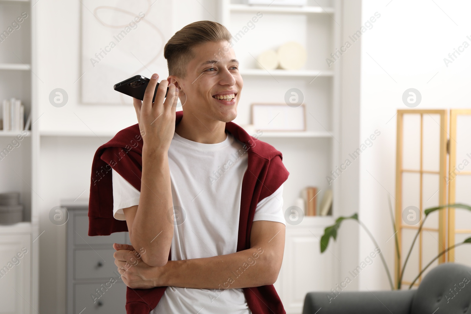 Photo of Young man with smartphone listening to voice message at home