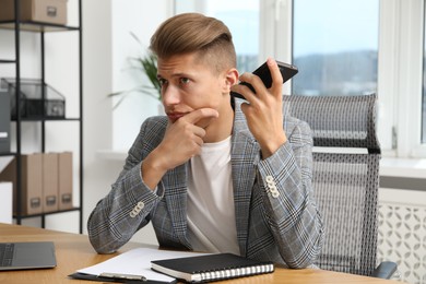 Photo of Young man with smartphone listening to voice message in office