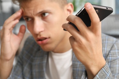 Photo of Young man with smartphone listening to voice message in office, selective focus