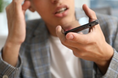 Photo of Young man recording voice message via smartphone in office, closeup
