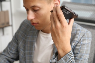Photo of Young man with smartphone listening to voice message in office, selective focus
