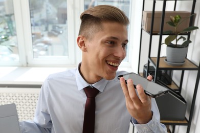 Photo of Young man recording voice message via smartphone in office