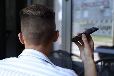 Photo of Young man with smartphone listening to voice message in outdoor cafe, back view