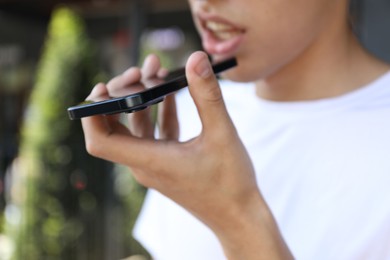 Photo of Young man recording voice message via smartphone outdoors, closeup