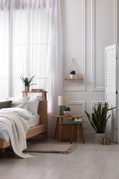 Stylish living room interior with bed, bedside tables, lamp and houseplants