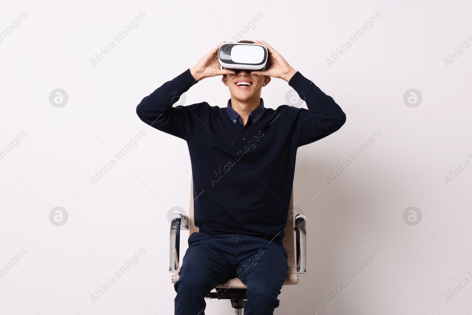 Photo of Happy young man with virtual reality headset sitting on chair near white wall