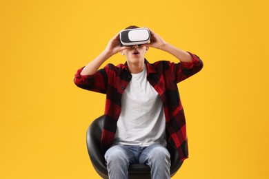 Photo of Emotional young man with virtual reality headset sitting on chair against yellow background