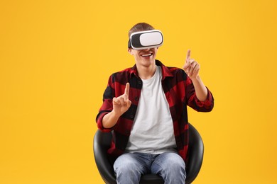 Photo of Happy young man with virtual reality headset sitting on chair against yellow background
