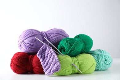 Many soft skeins of yarn, knitted fabric and needles on light grey background