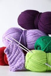 Many soft skeins of yarn, knitted fabric and needles on light grey background, closeup