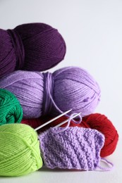 Many soft skeins of yarn, knitted fabric and needles on light grey background, closeup