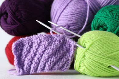 Many soft skeins of yarn, knitted fabric and needles on light grey background, closeup