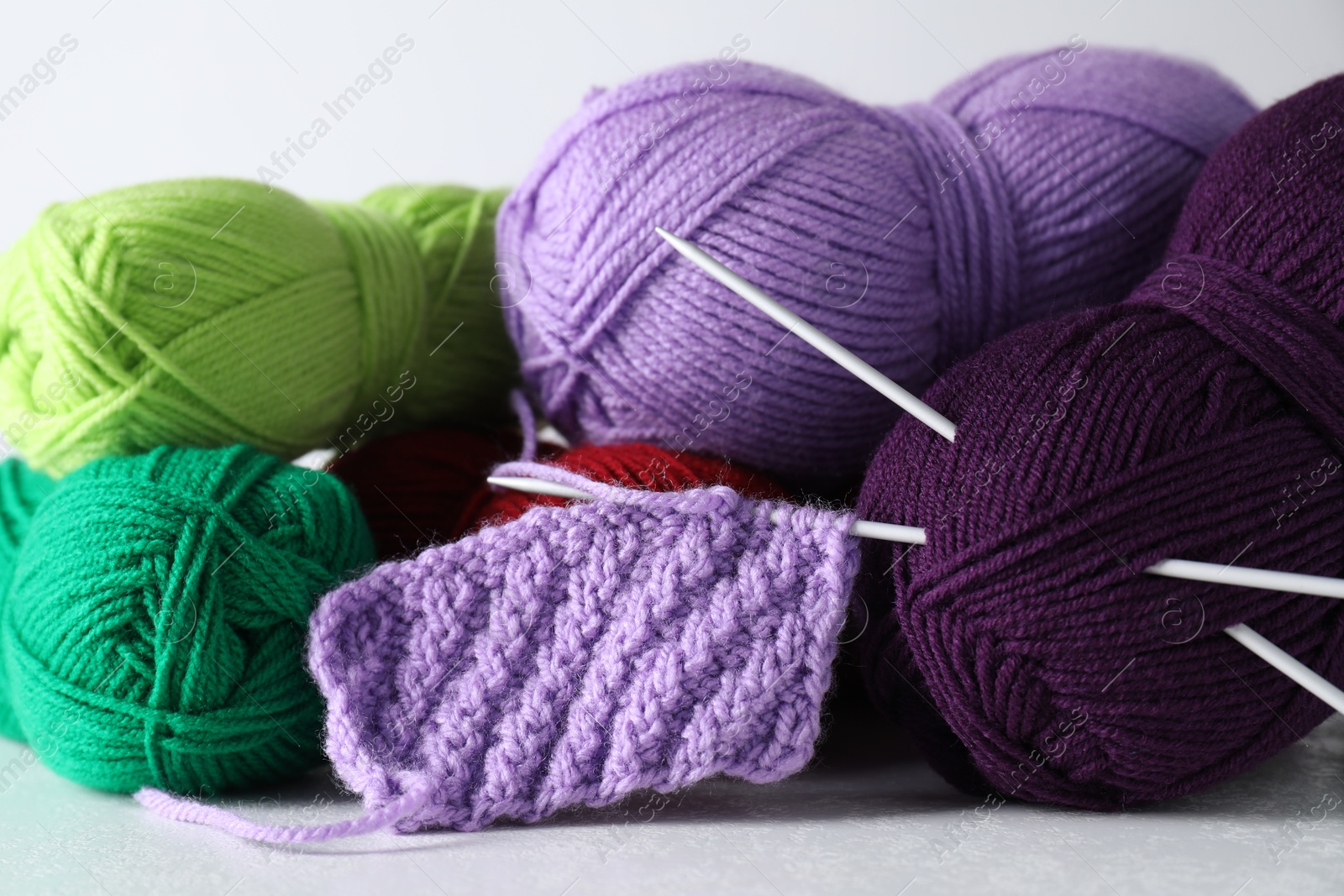 Photo of Many soft skeins of yarn, knitted fabric and needles on light grey background, closeup