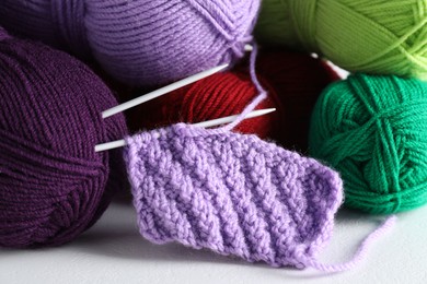 Photo of Many soft skeins of yarn, knitted fabric and needles on light grey background, closeup