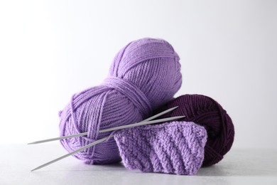 Skeins of yarn, knitted fabric and needles on light grey background