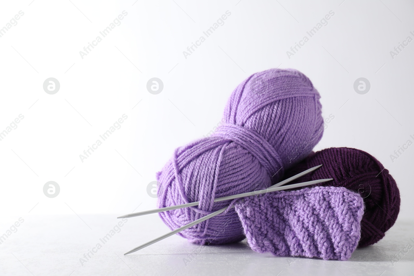 Photo of Skeins of yarn, knitted fabric and needles on light grey background, space for text