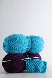 Skeins of yarn, knitted fabric and needles on light grey background