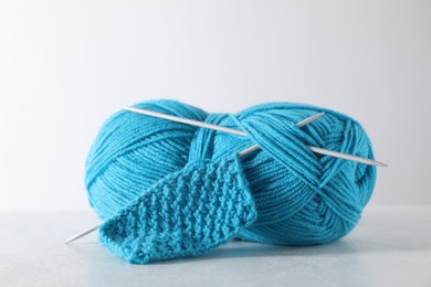 Skein of light blue yarn, knitted fabric and needles on light grey background