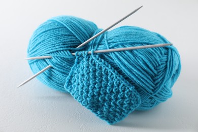 Photo of Skein of light blue yarn, knitted fabric and needles on light grey background