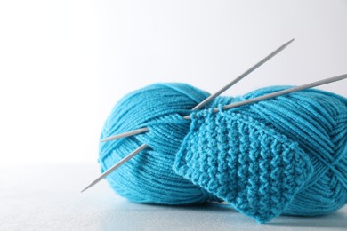 Skein of light blue yarn, knitted fabric and needles on light grey background, closeup