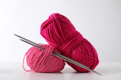 Photo of Two soft skeins of yarn and knitting needles on light grey background