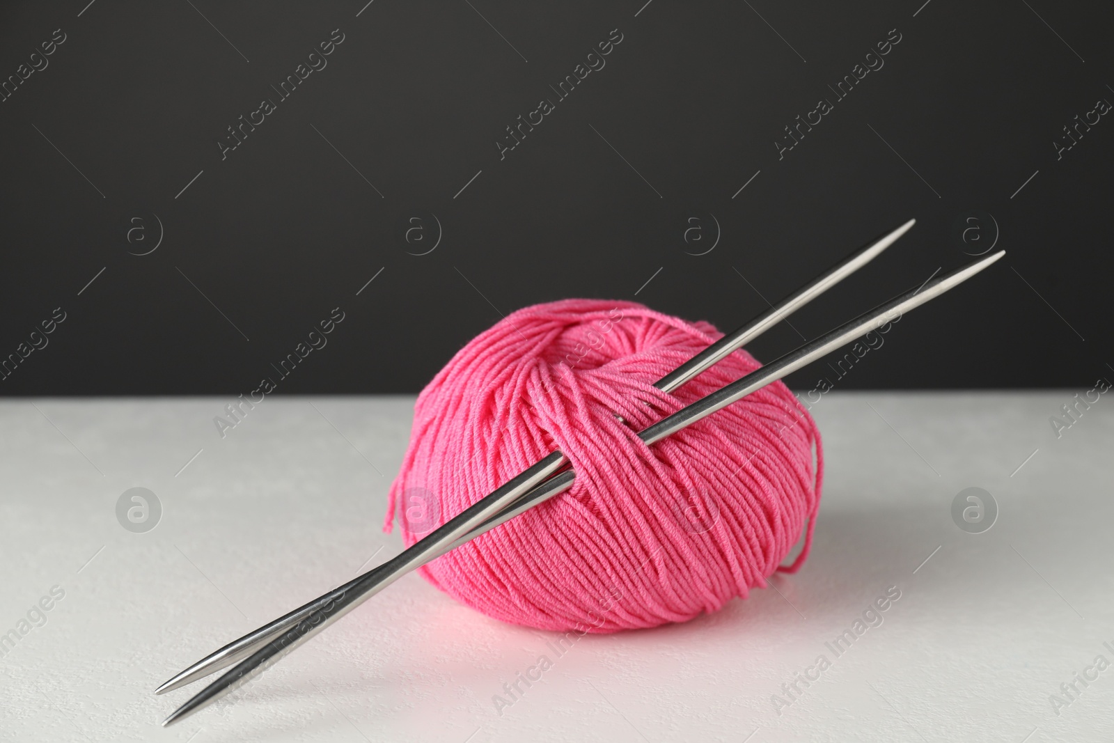 Photo of Pink skein of yarn and knitting needles on white table against grey background