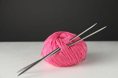 Pink skein of yarn and knitting needles on white table against grey background