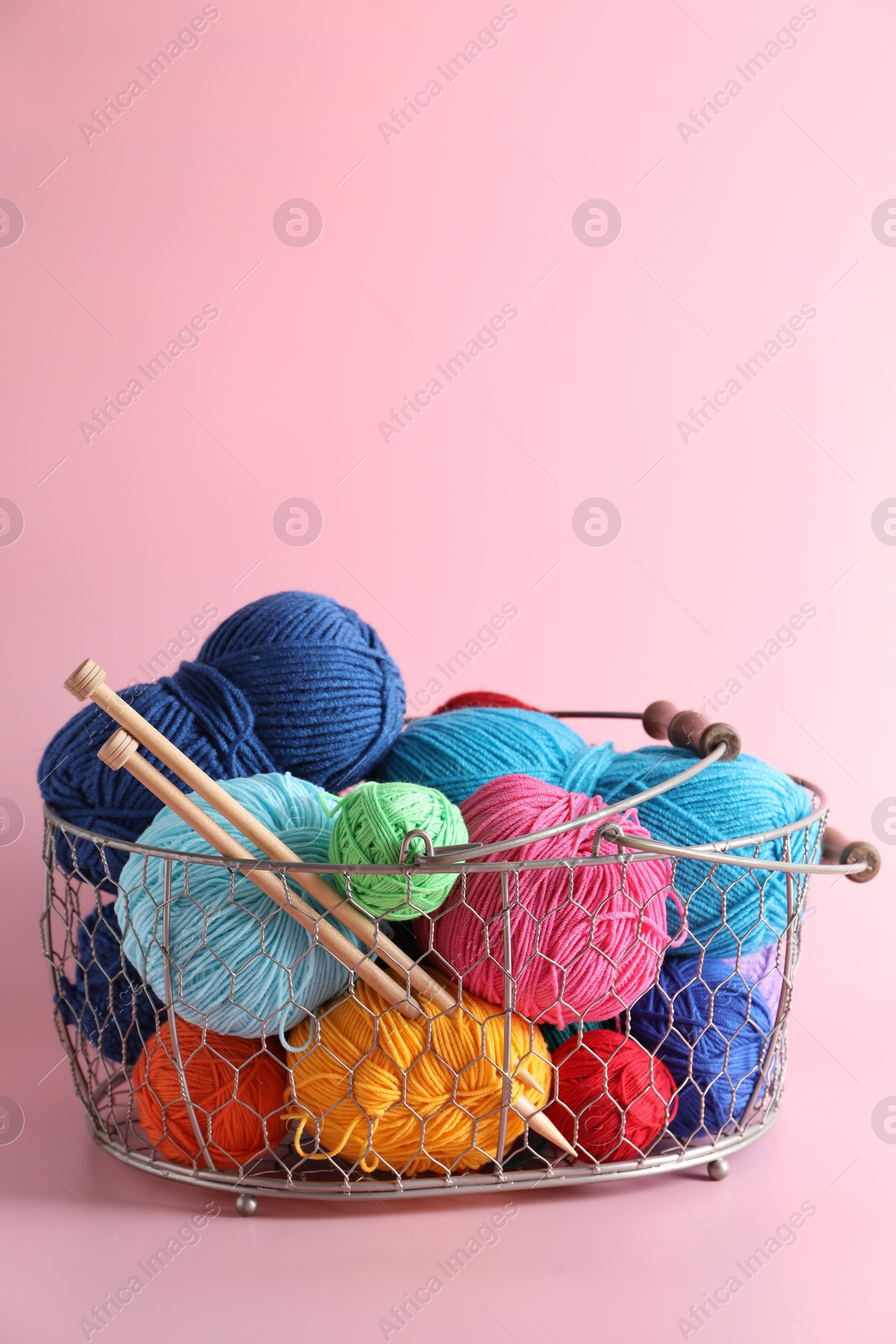 Photo of Metal basket with bright yarns and knitting needles on pink background. Space for text