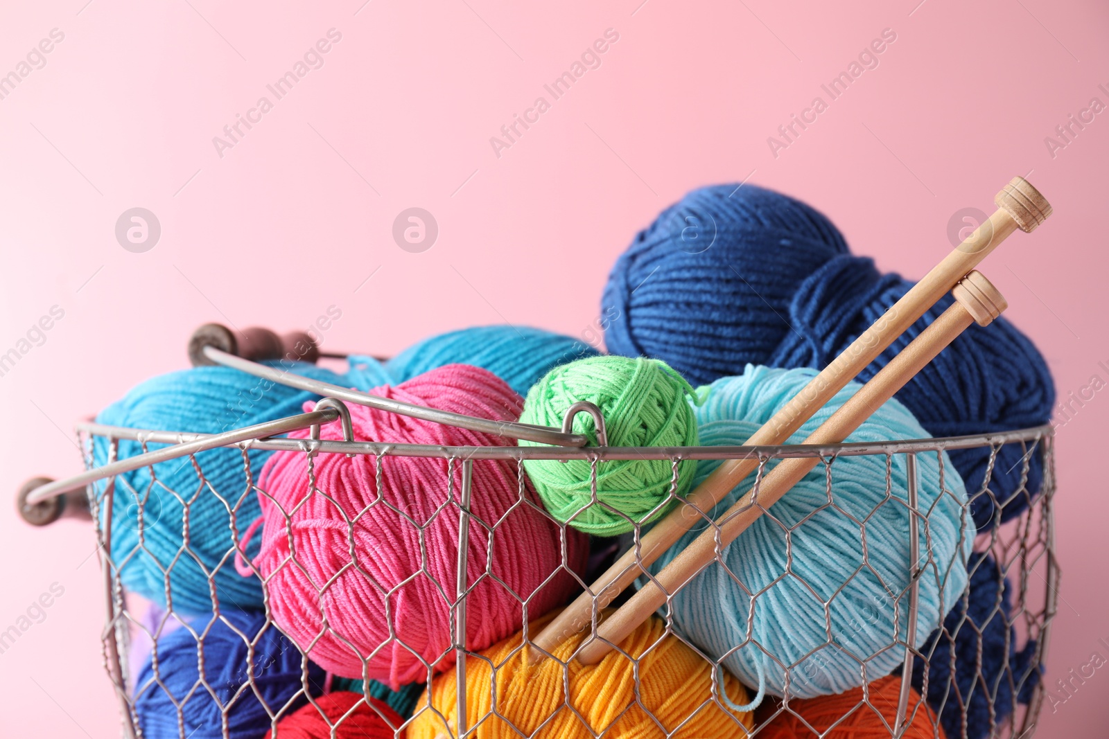 Photo of Metal basket with bright yarns and knitting needles on pink background, closeup