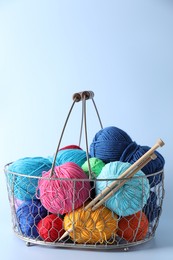 Metal basket with bright yarns and knitting needles on light blue background