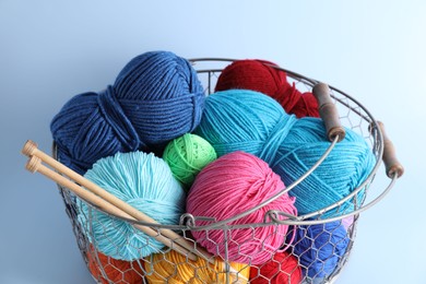 Photo of Metal basket with bright yarns and knitting needles on light blue background, closeup