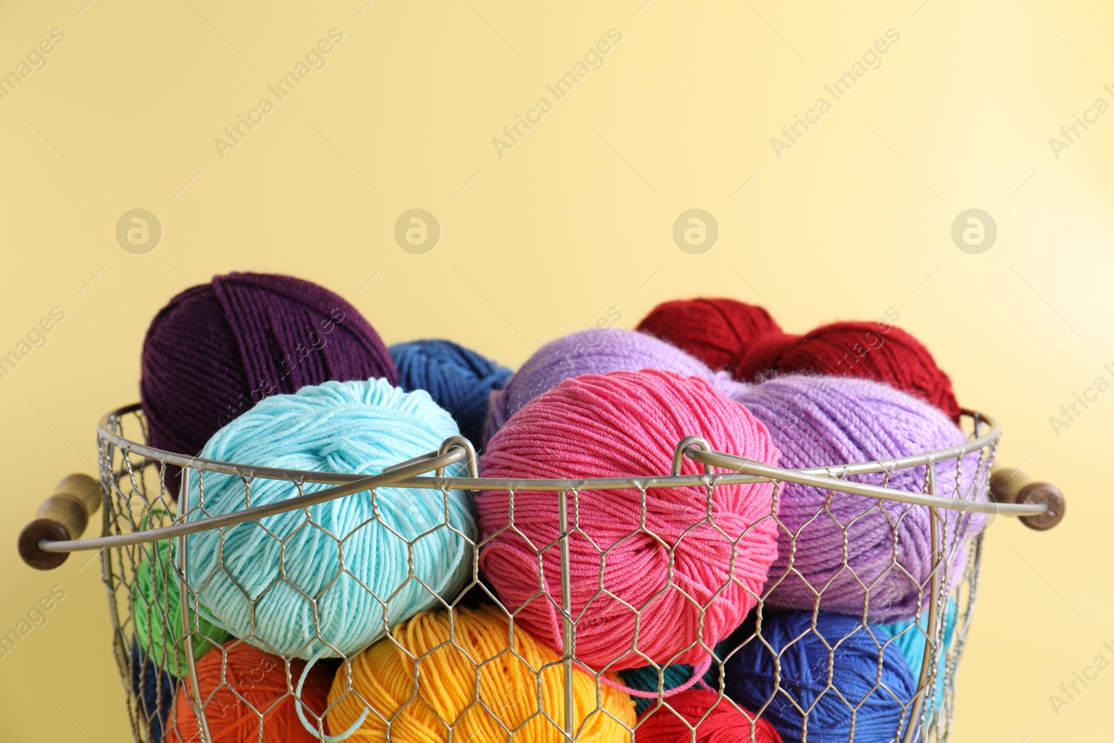 Photo of Metal basket with bright yarns on yellow background, closeup