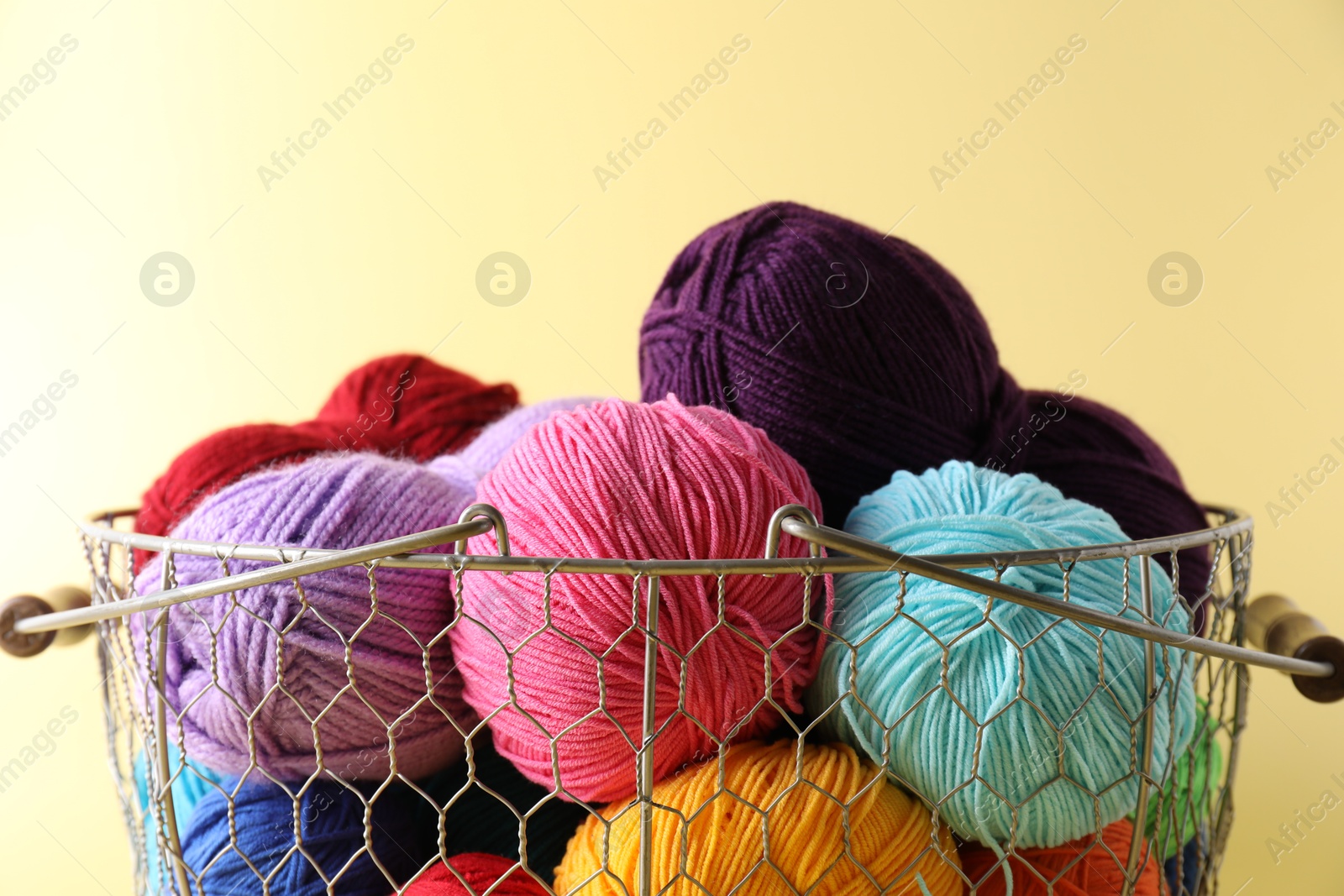 Photo of Metal basket with bright yarns on yellow background, closeup