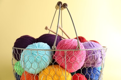 Photo of Metal basket with bright yarns on yellow background, closeup