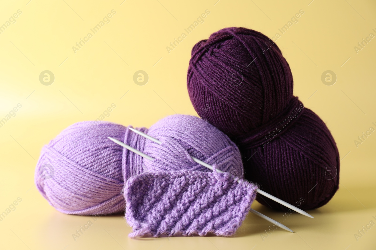 Photo of Skeins of yarn, knitting needles and pattern sample on yellow background, closeup