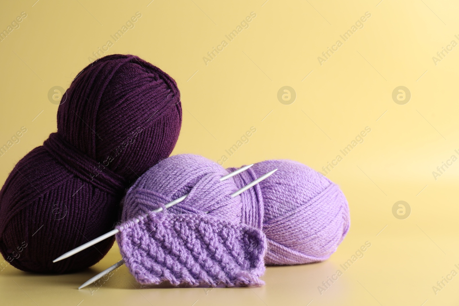 Photo of Skeins of yarn, knitting needles and pattern sample on yellow background, closeup. Space for text