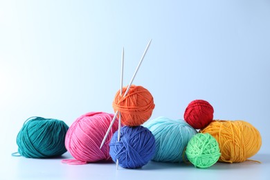 Colorful yarns and knitting needles on light background