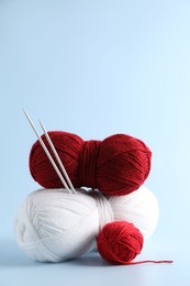 Colorful yarns and knitting needles on light background