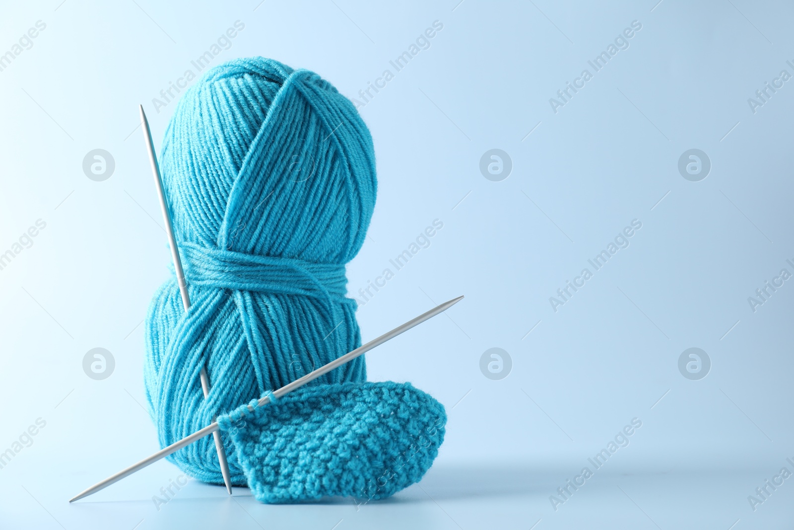 Photo of Skein of yarn, knitting needles and pattern sample on light background. Space for text